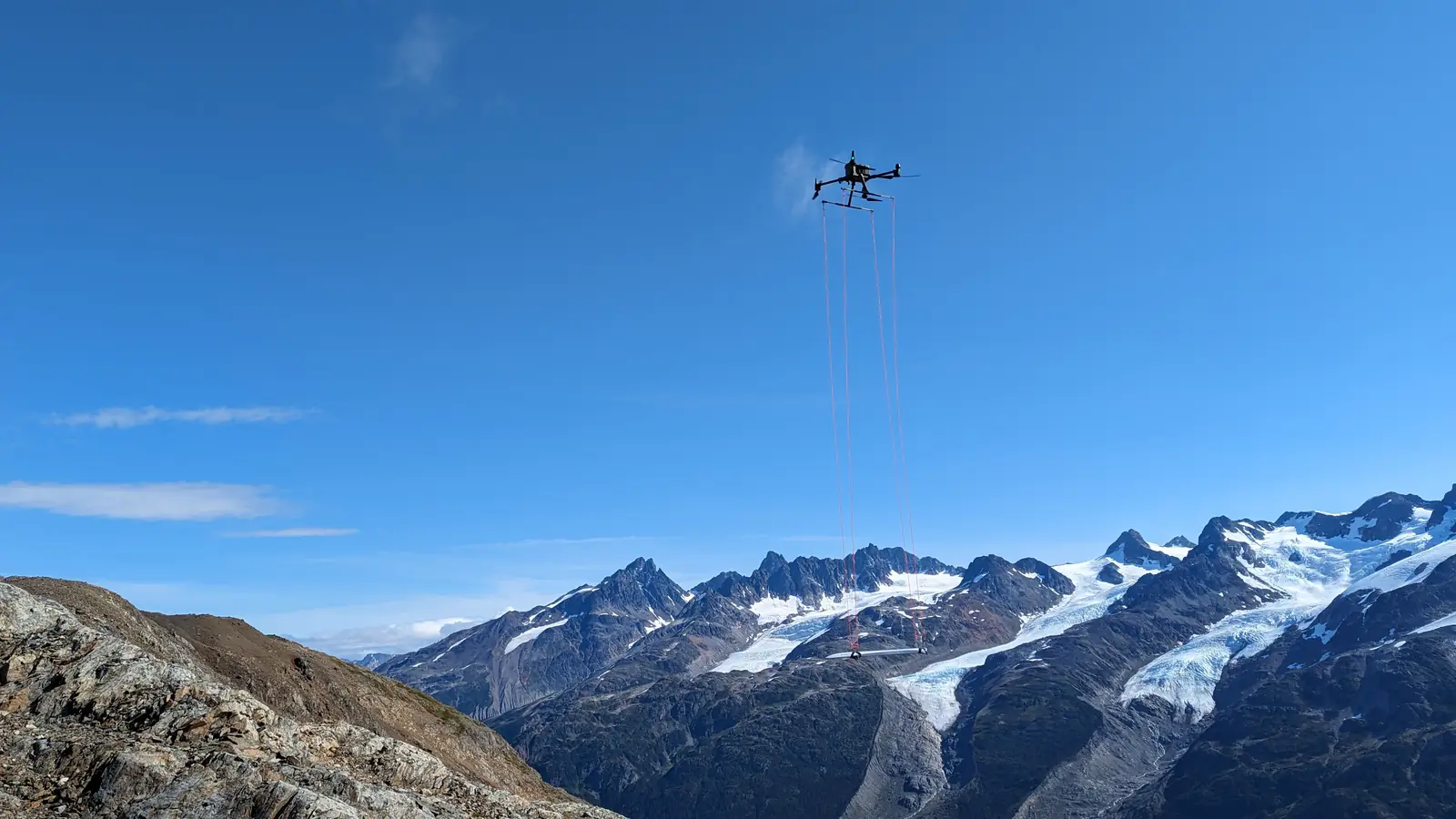 Drone con magnetómetro suspendido en vuelo frente a picos glaciares de alta montaña