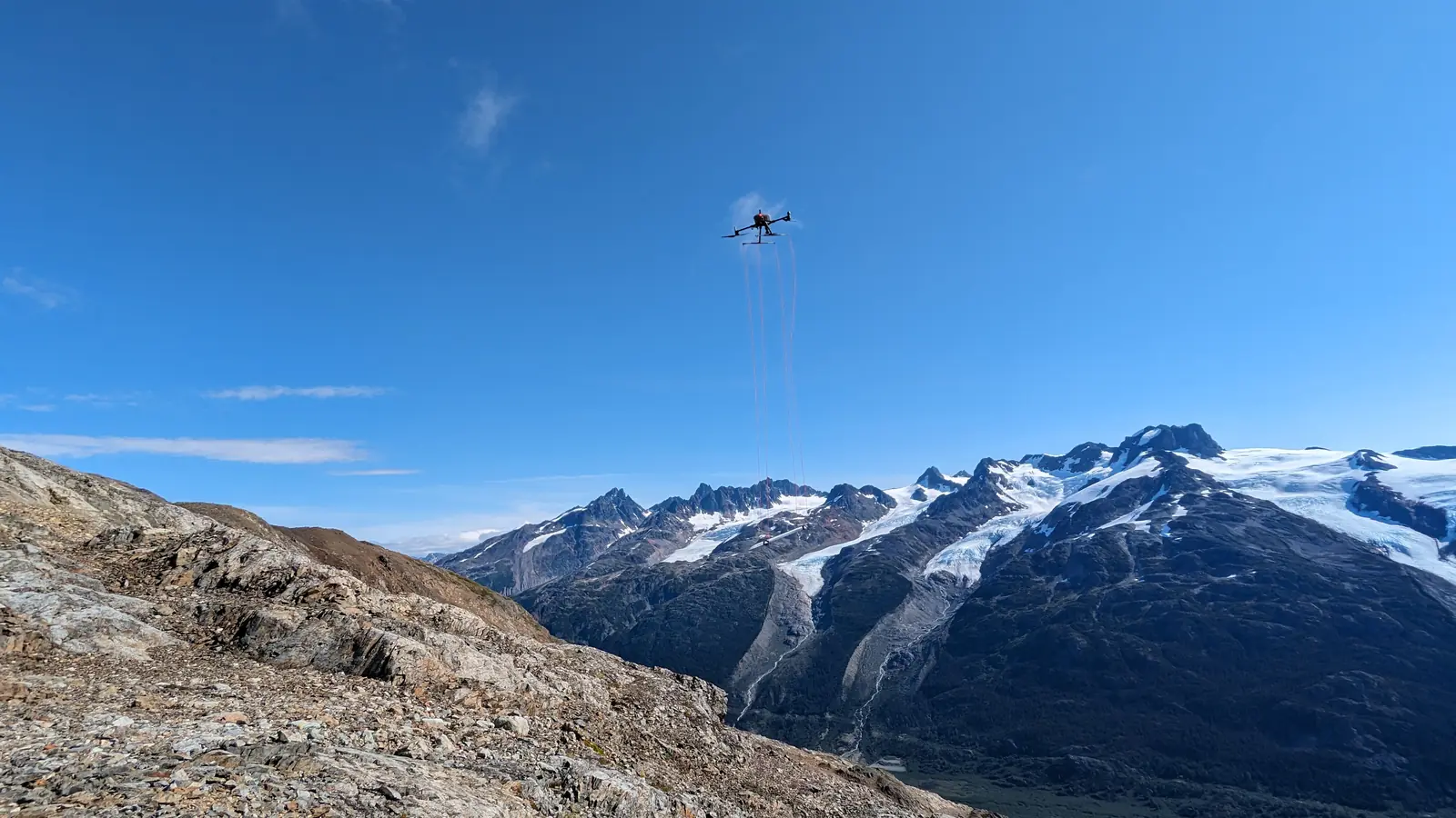 Drone de Rosor en vuelo con magnetómetro remolcado por cables, sobre terreno glaciar de alta montaña